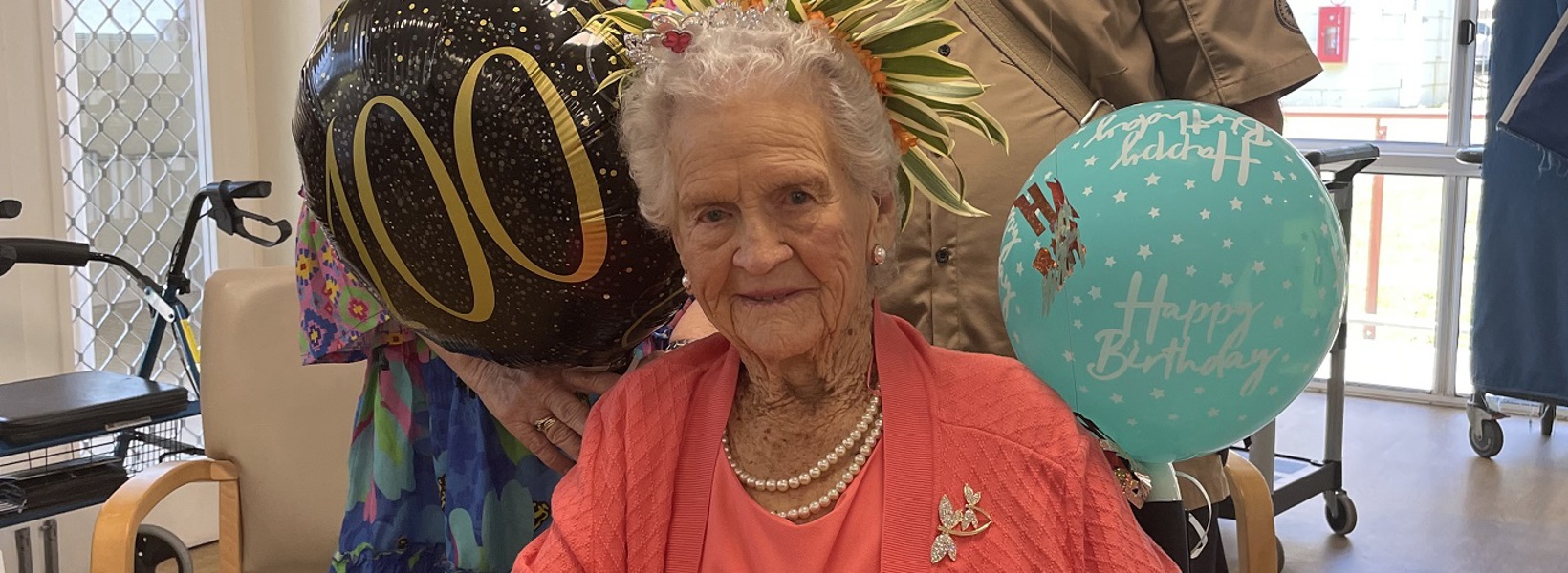 Lady in pink smiles at the camera with birthday balloons in the background Lady in pink smiles at the camera with birthday balloons in the background